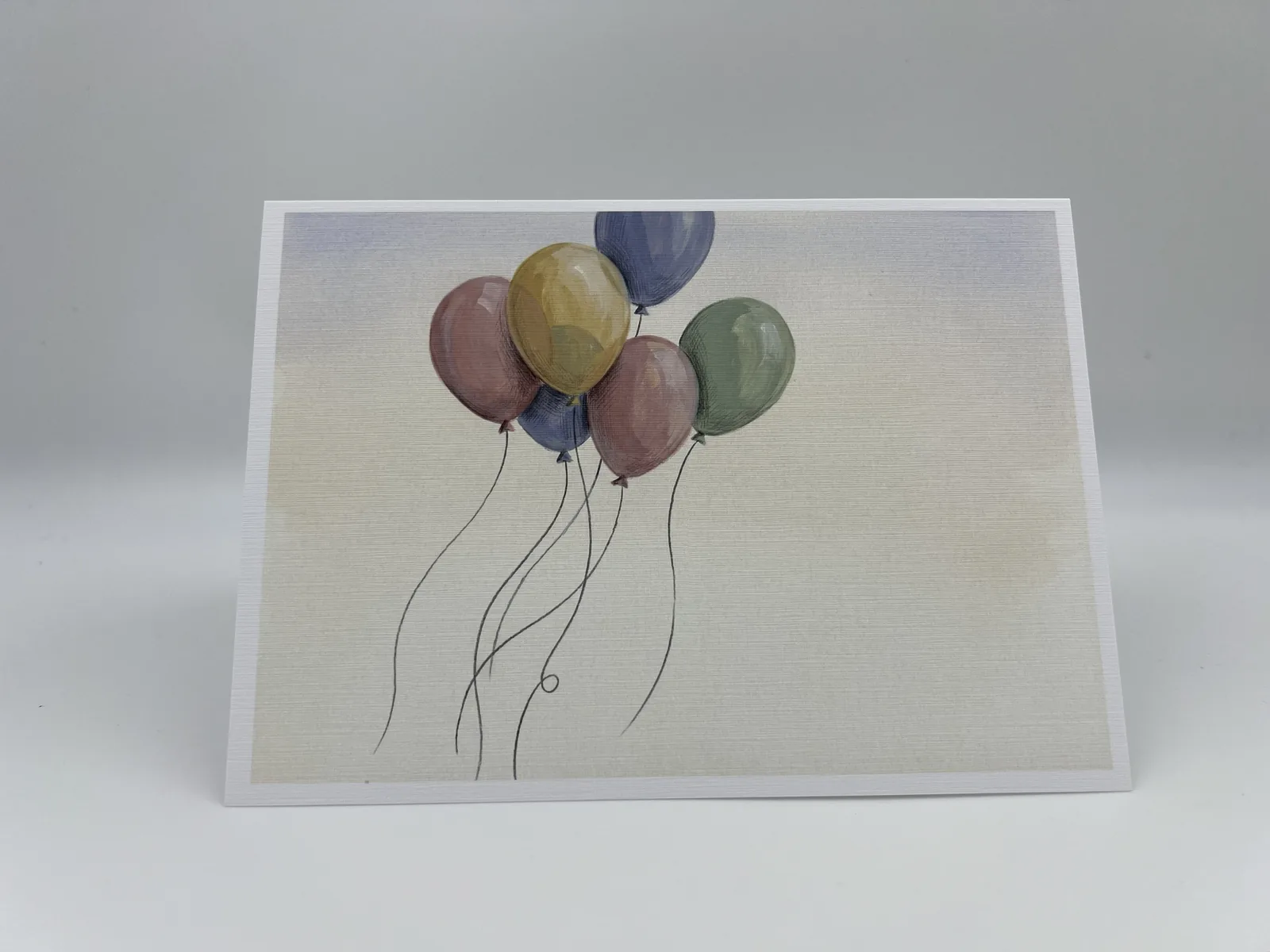 A birthday card with a bunch of pastel watercolor balloons drifting on trailing strings