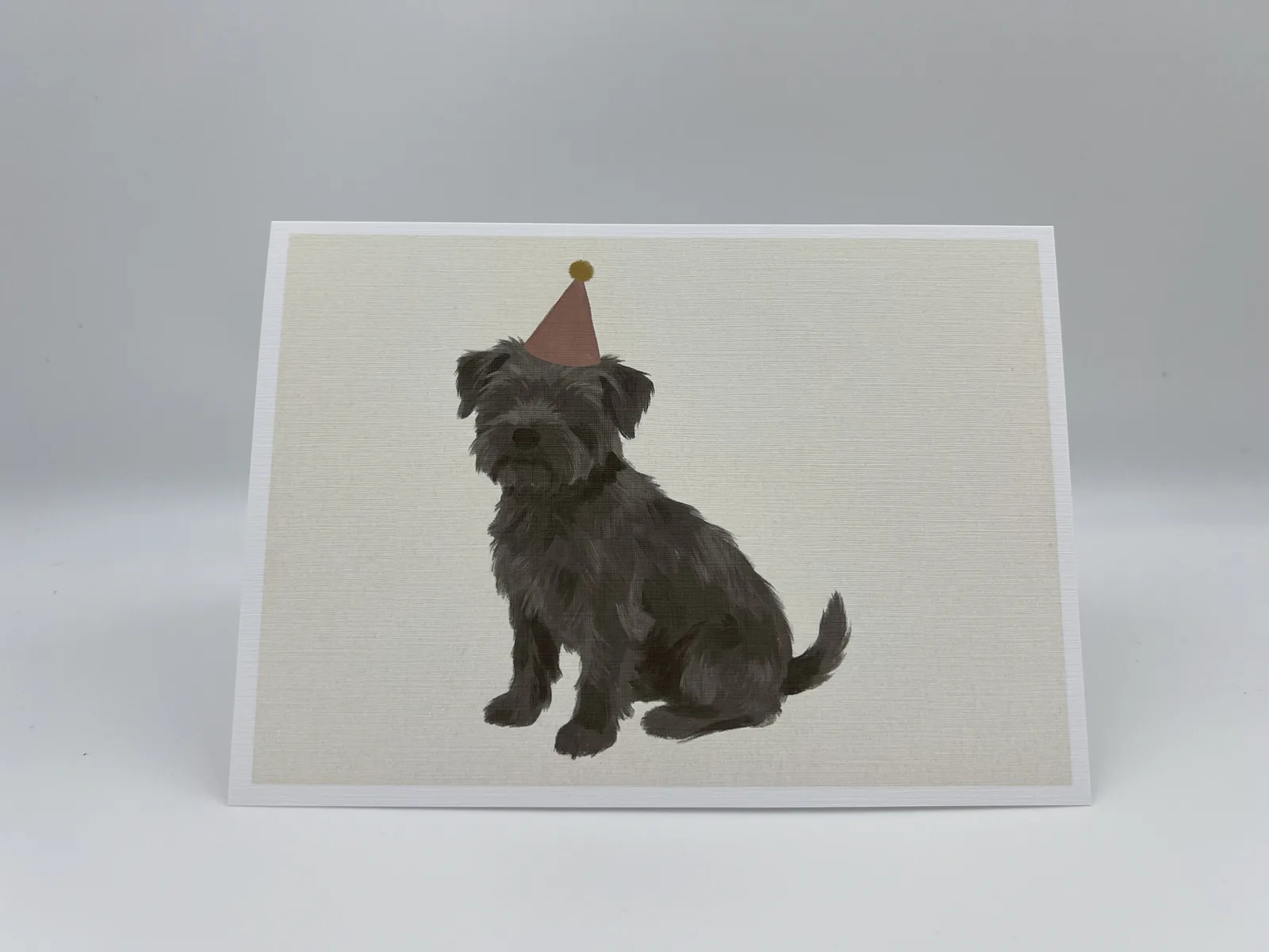 A birthday card featuring a scruffy dog wearing a party hat