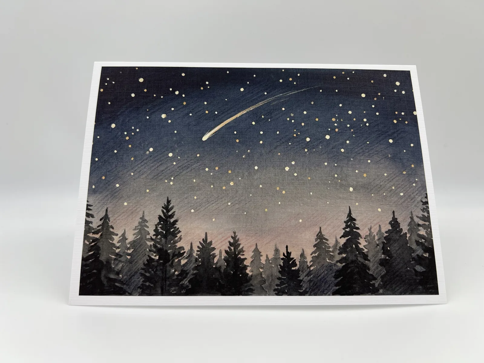A birthday card showing a starry night sky with a shooting star over a pine forest