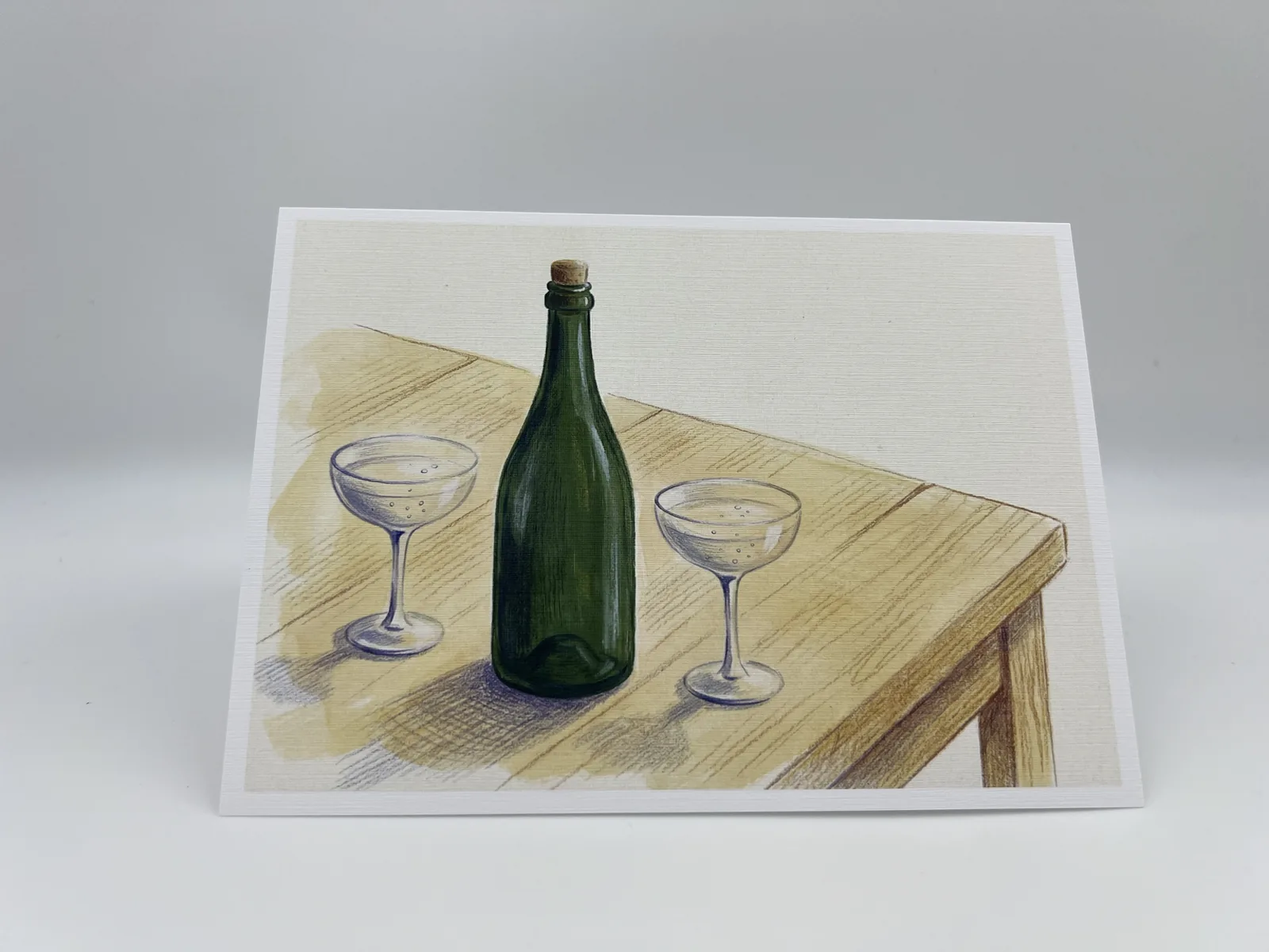A birthday card illustrated with a wine bottle and two glasses on a wooden table