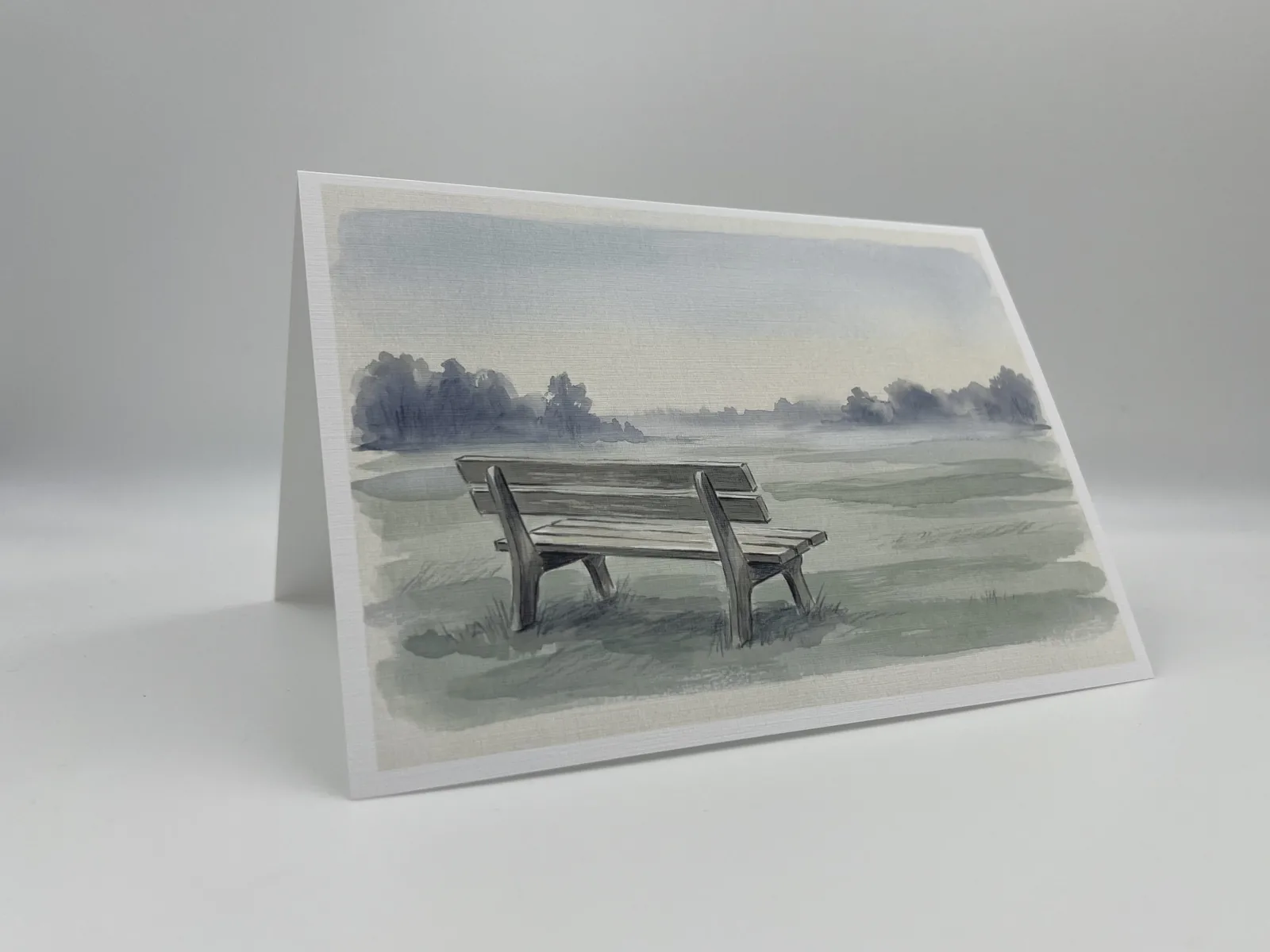 A sympathy card illustrated with an empty wooden bench beside a misty meadow
