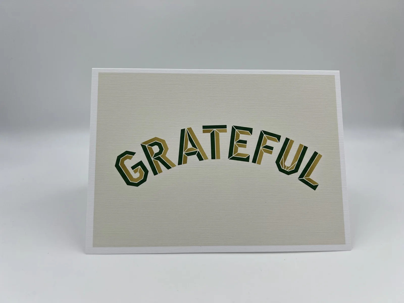 A thank-you card with "Grateful" in arched green-and-gold varsity lettering on an ivory background